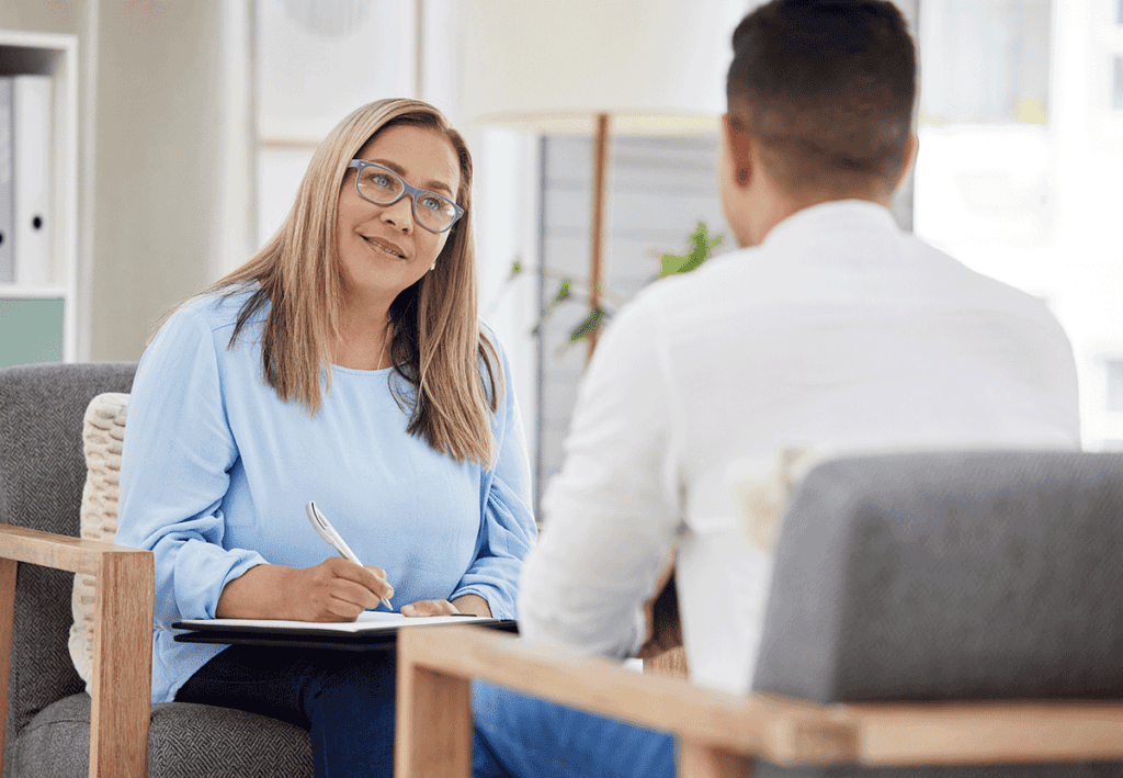 Friendly blonde therapist wearing blue shirt and glasses providing a client with examples of cognitive behavioral therapy