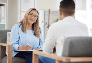 Friendly blonde therapist wearing blue shirt and glasses providing a client with examples of cognitive behavioral therapy