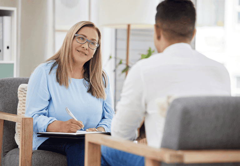 Friendly blonde therapist wearing blue shirt and glasses providing a client with examples of cognitive behavioral therapy